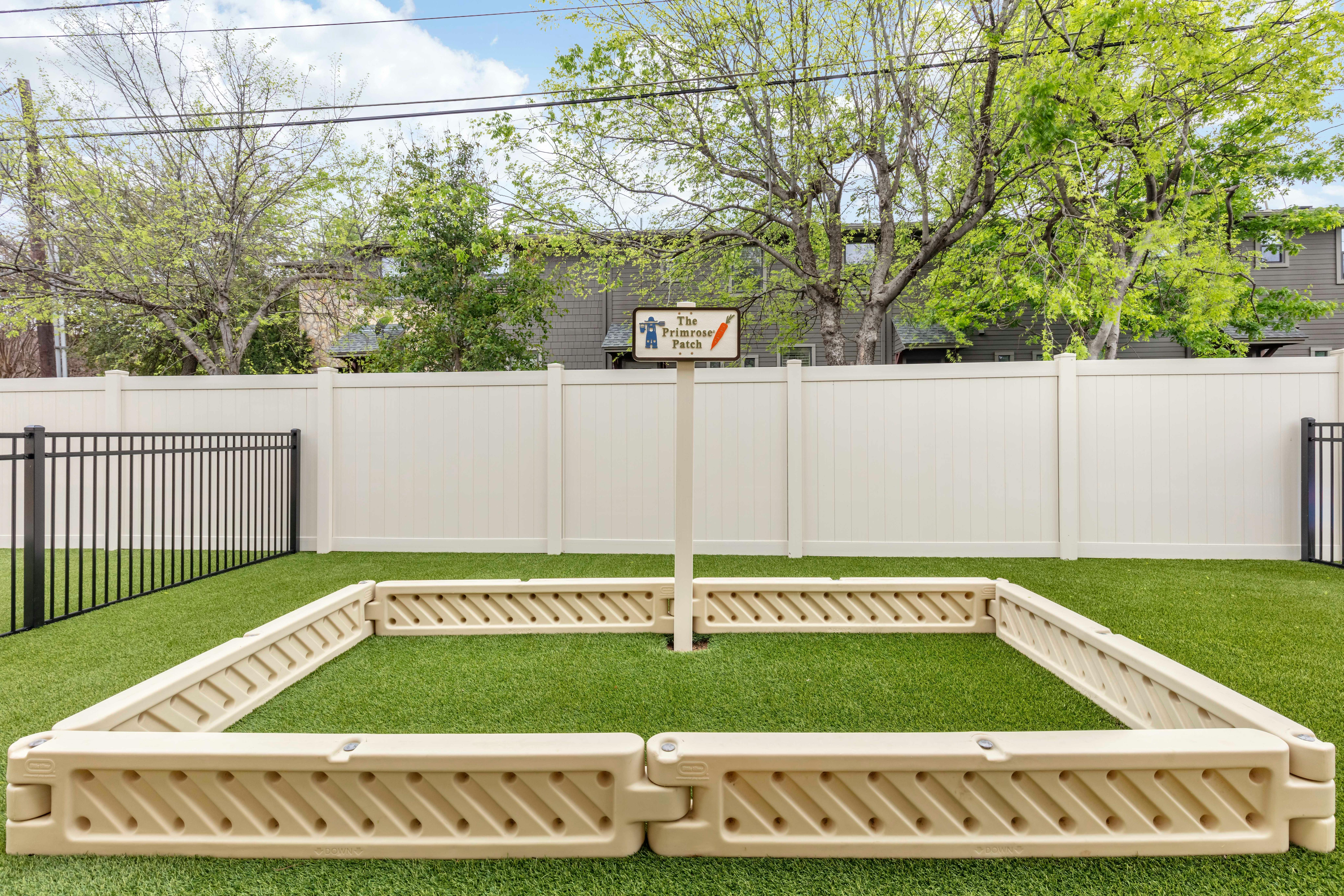 An outdoor play area with artificial grass and a low tan fence around a center post