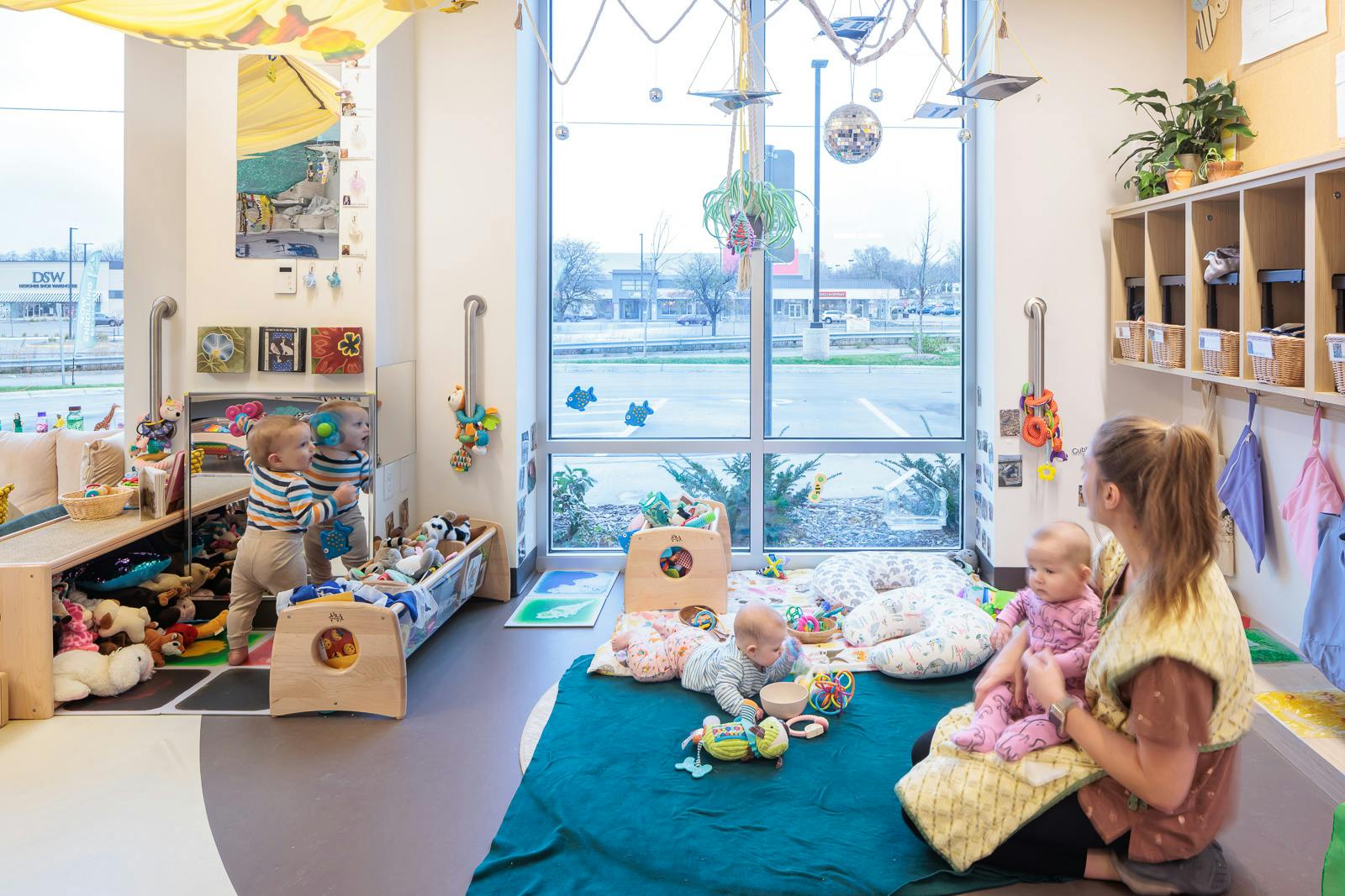 Person sitting with a child, another child on the floor, and a child standing
