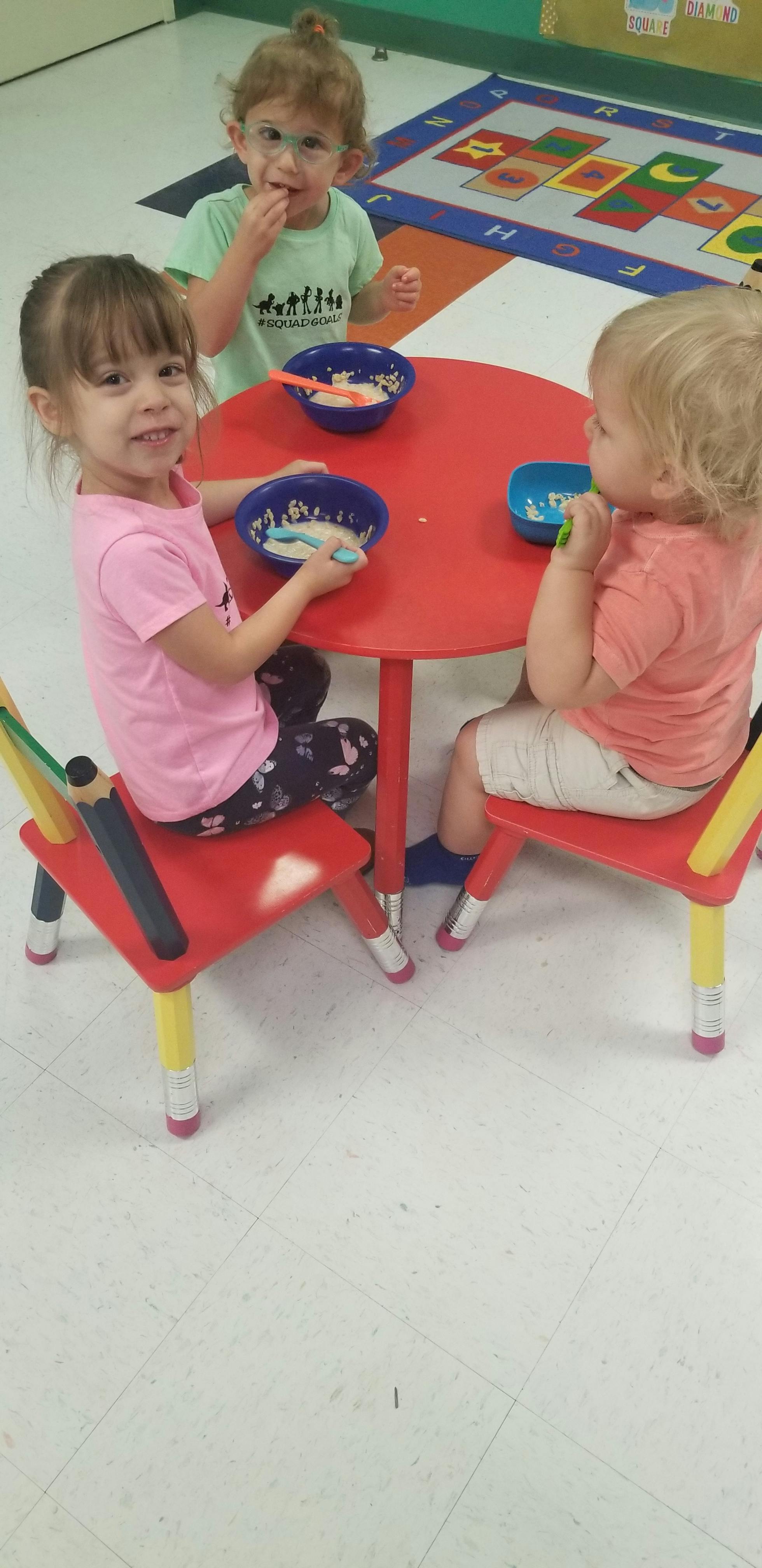 Three children eating at a small red table