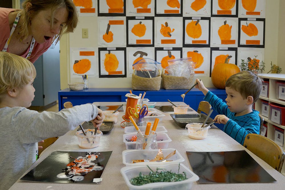 Person watching two children painting at a table in a classroom