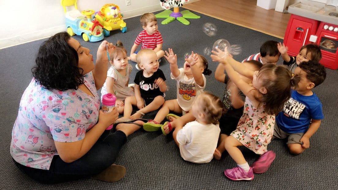 Adult and multiple children sitting on floor playing with bubbles