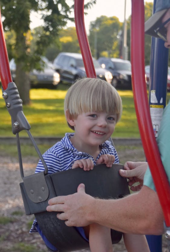 Child in a swing with a person's hands on the swing