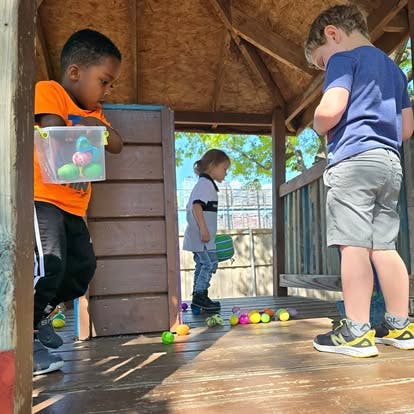 Three children playing with colorful plastic eggs in a wooden outdoor playhouse