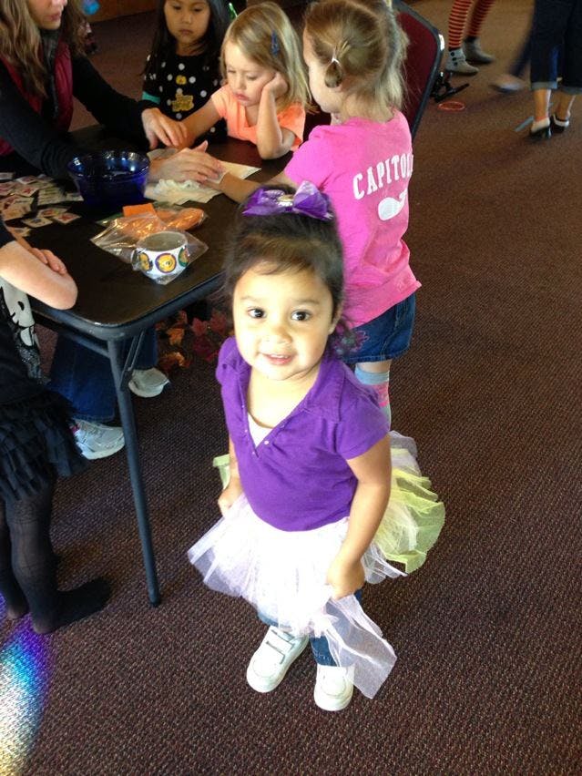 Child in purple shirt and white tutu standing in front of a table with other children