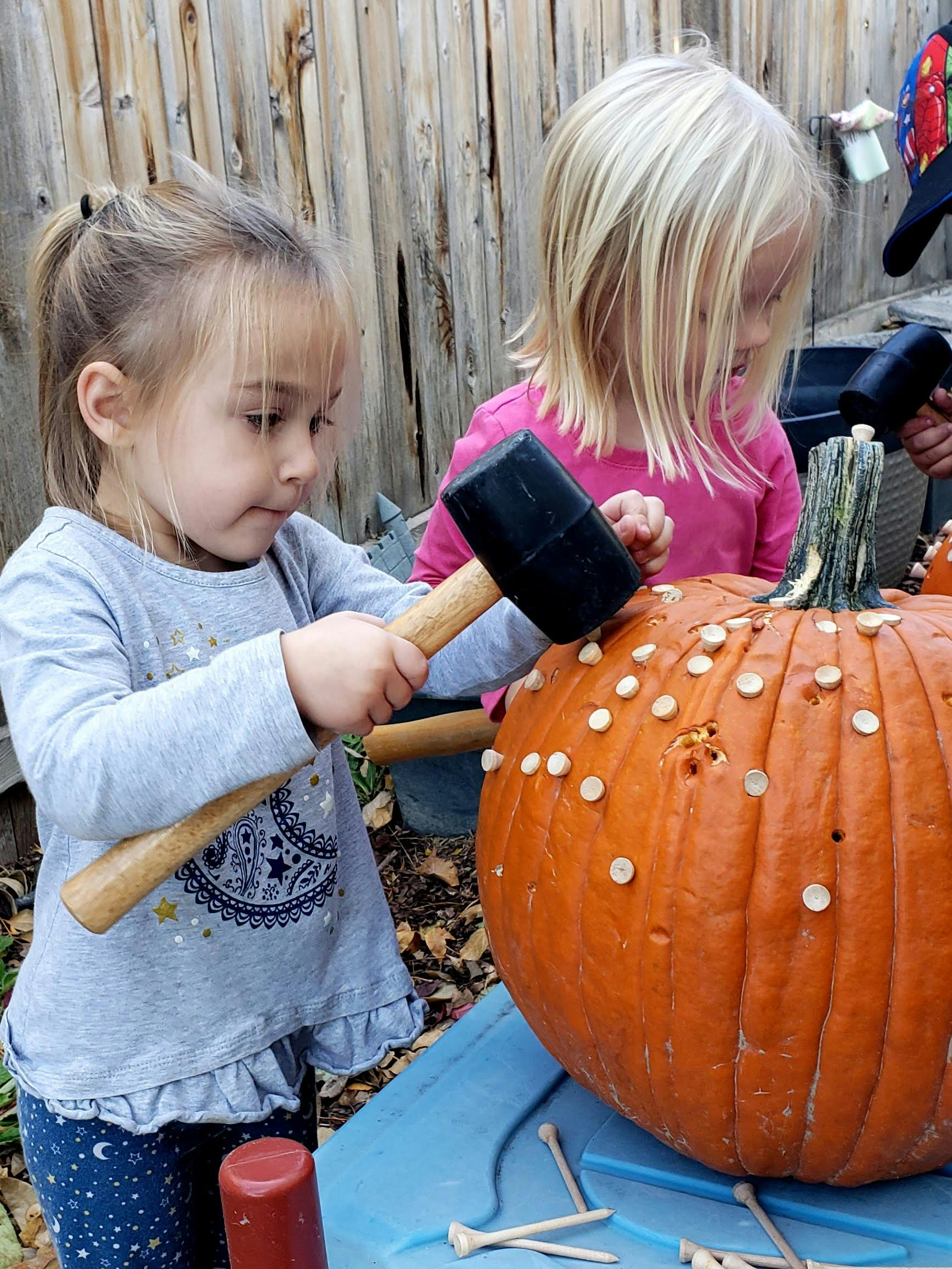 Two children hammering golf tees into a pumpkin