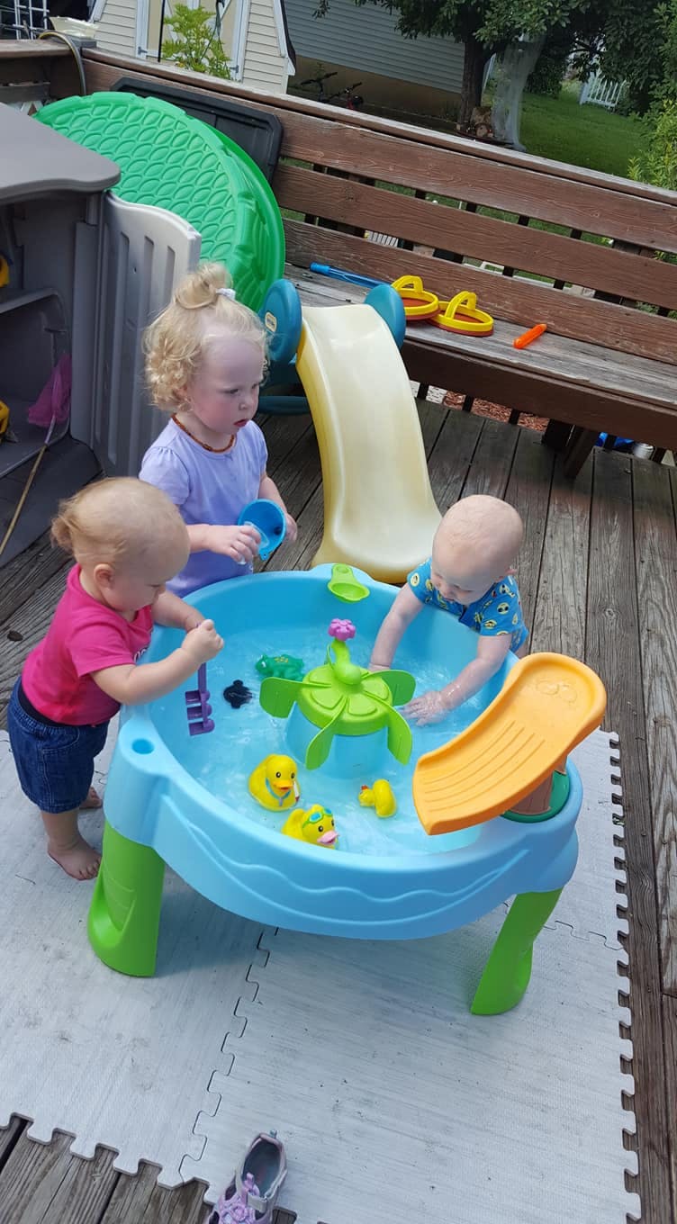 Three children playing with a water table on a deck
