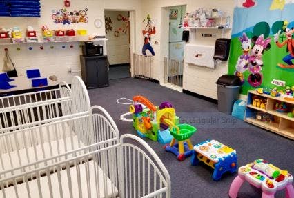 Two white cribs in a daycare room with colorful toys