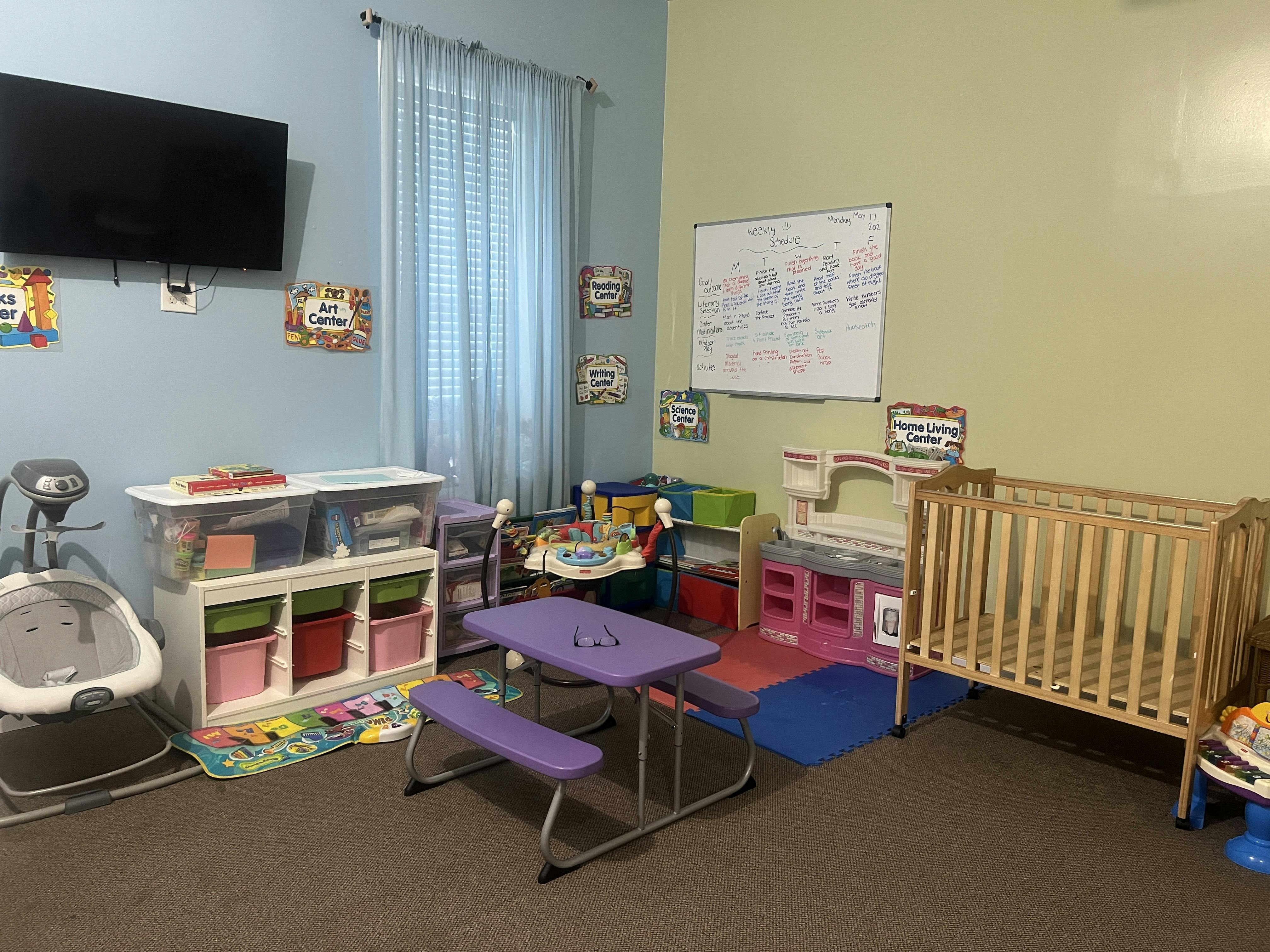 Classroom with play centers, a small table, crib, and TV