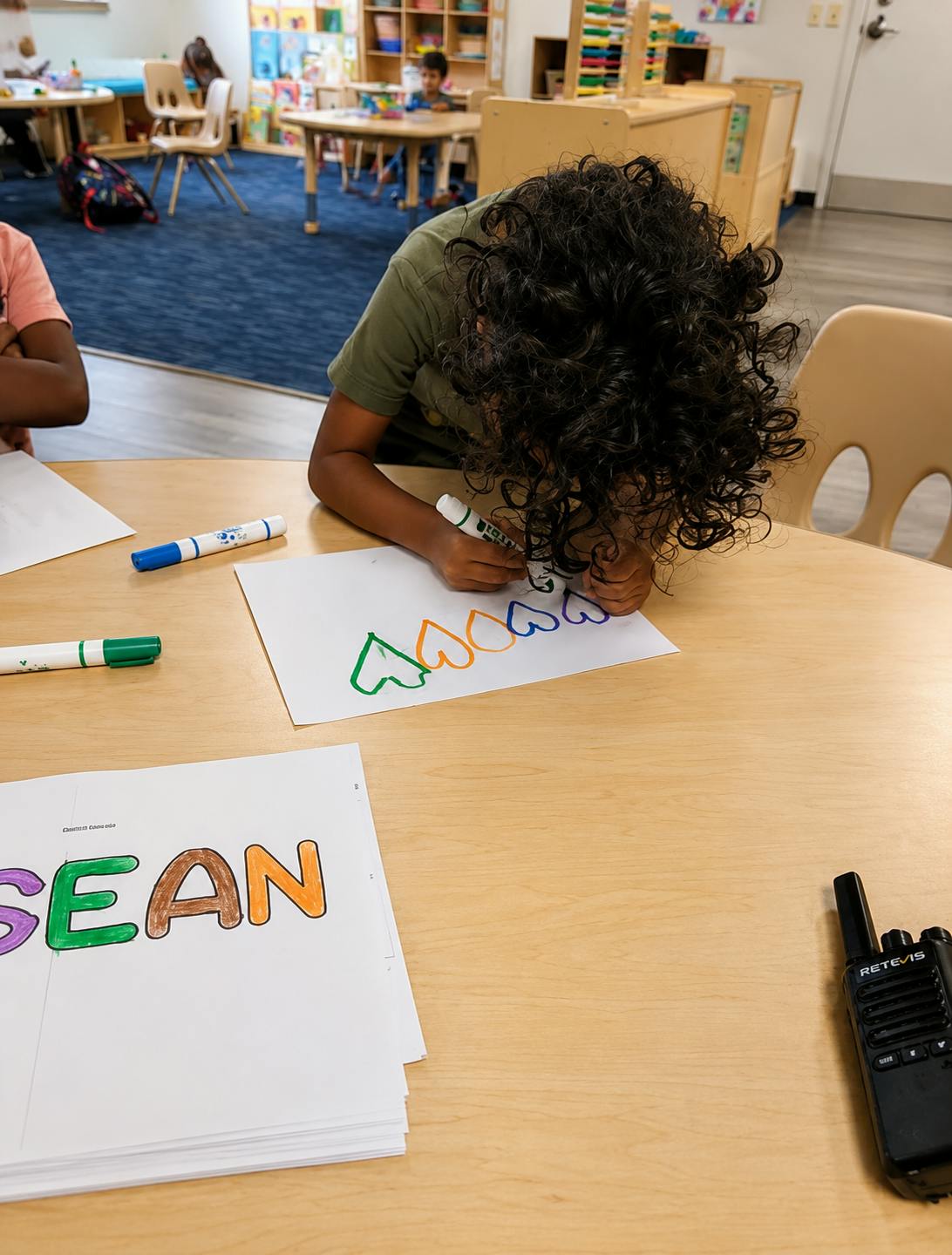 Child drawing hearts on paper at a desk in a classroom