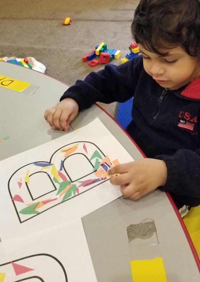 Child decorating a large letter B with colorful paper cutouts