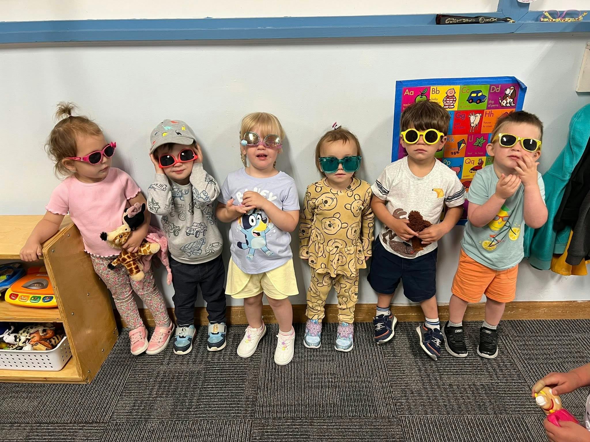 Six young children wearing sunglasses and standing in a row