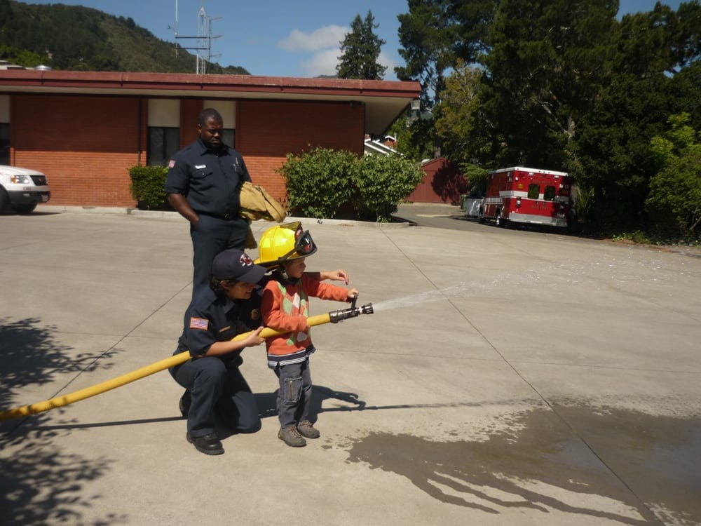 Adult and child in firefighter gear holding a hose, spraying water