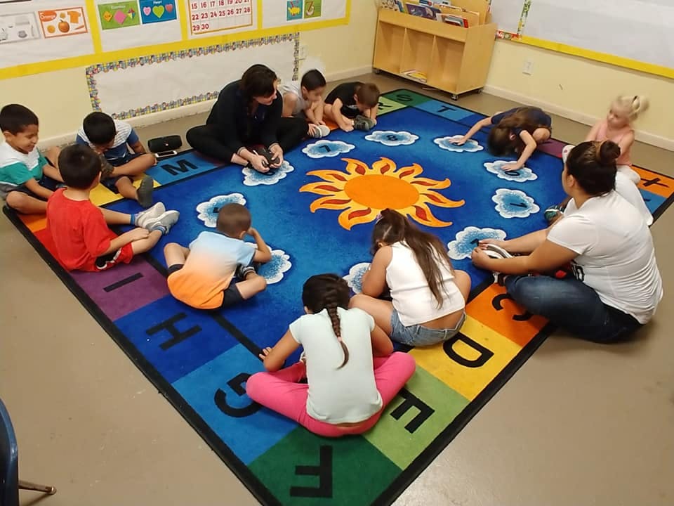 Adults and children sitting on a colorful rug in a classroom