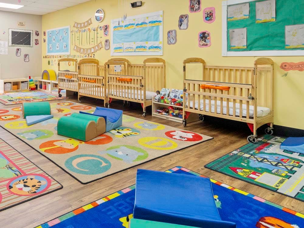 cribs in a daycare room with colorful rugs and play mats