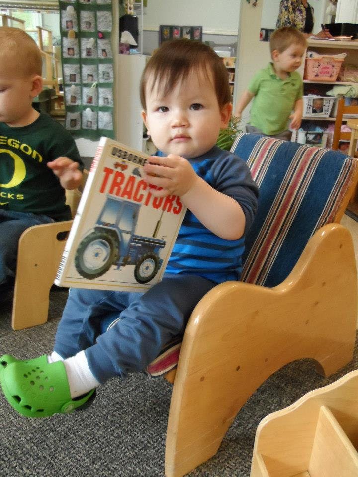 Child sitting in a chair holding a book titled "Tractors"