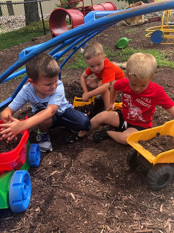 Three children playing with toy trucks in dirt