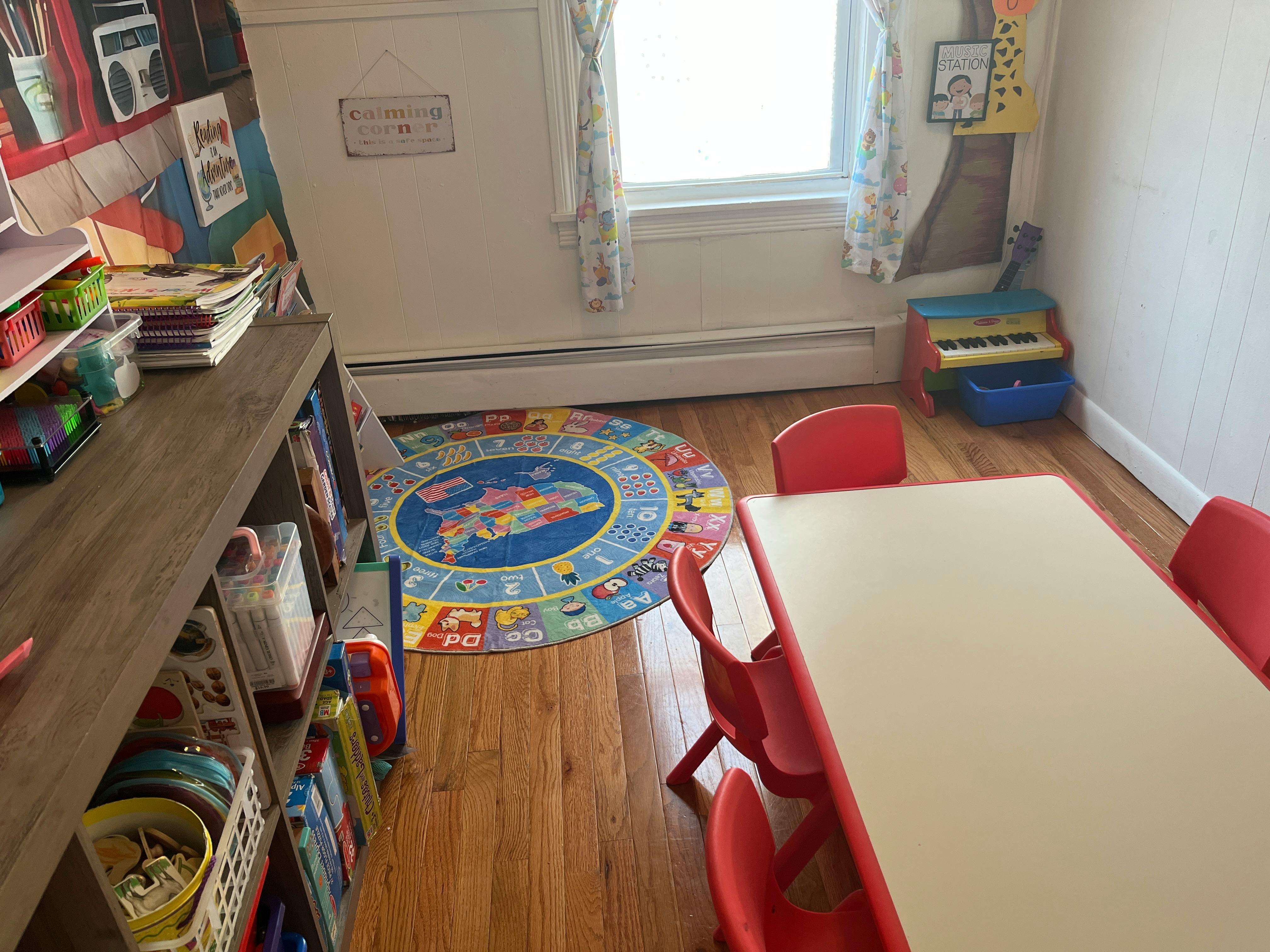 Children's play area with a table, red chairs, and a colorful alphabet rug