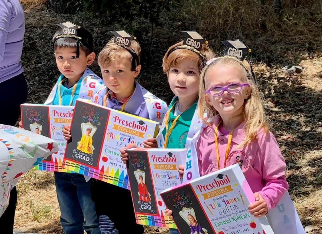 Four children wearing graduation headbands and holding preschool diplomas