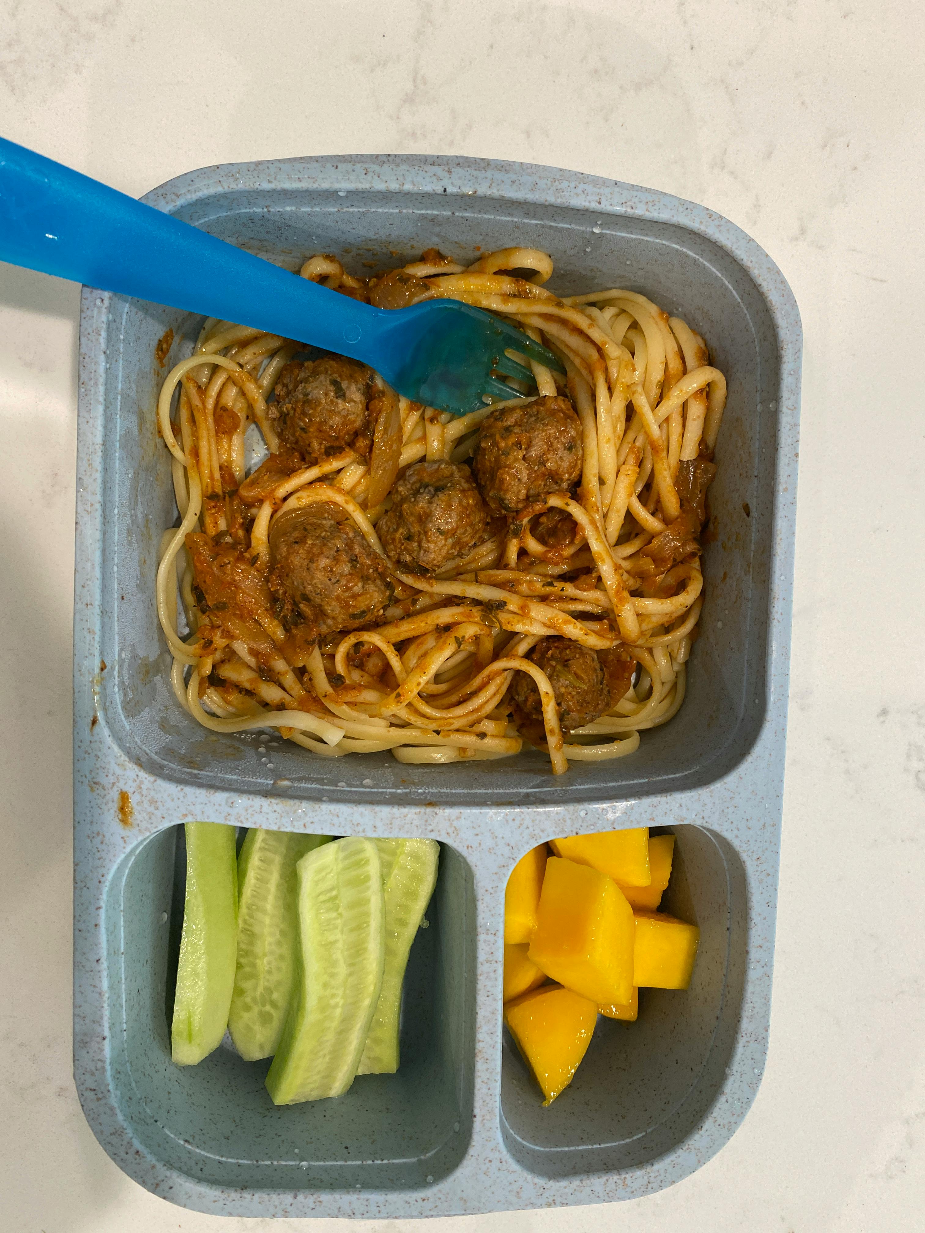 Spaghetti and meatballs with cucumber slices and mango in a divided container