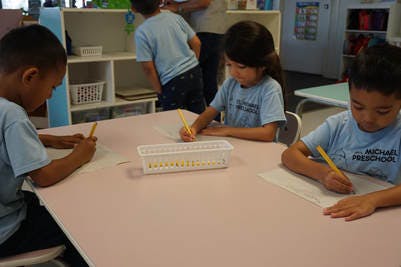 Three children drawing at a table in a classroom