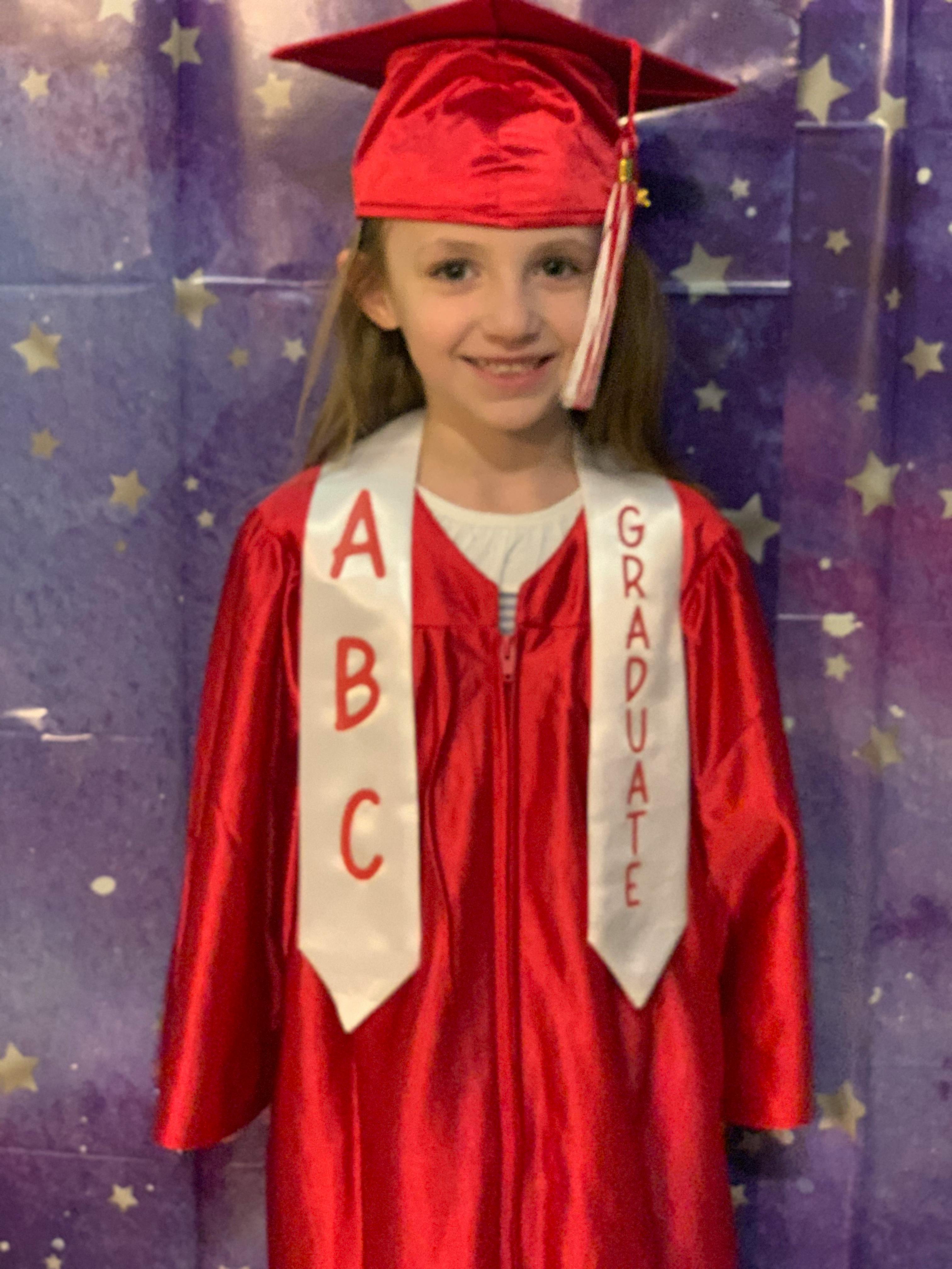 Child in red graduation cap and gown with ABC and Graduate sashes