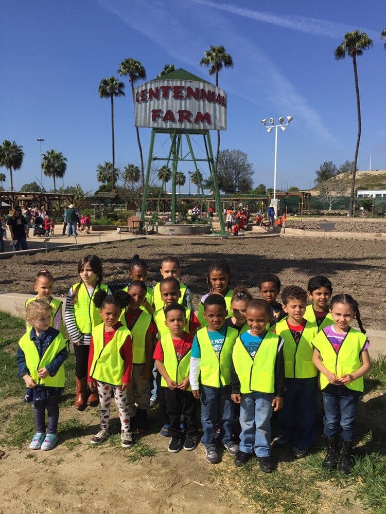 Children in neon vests in front of a water tower with "Centennial Farm" written on it