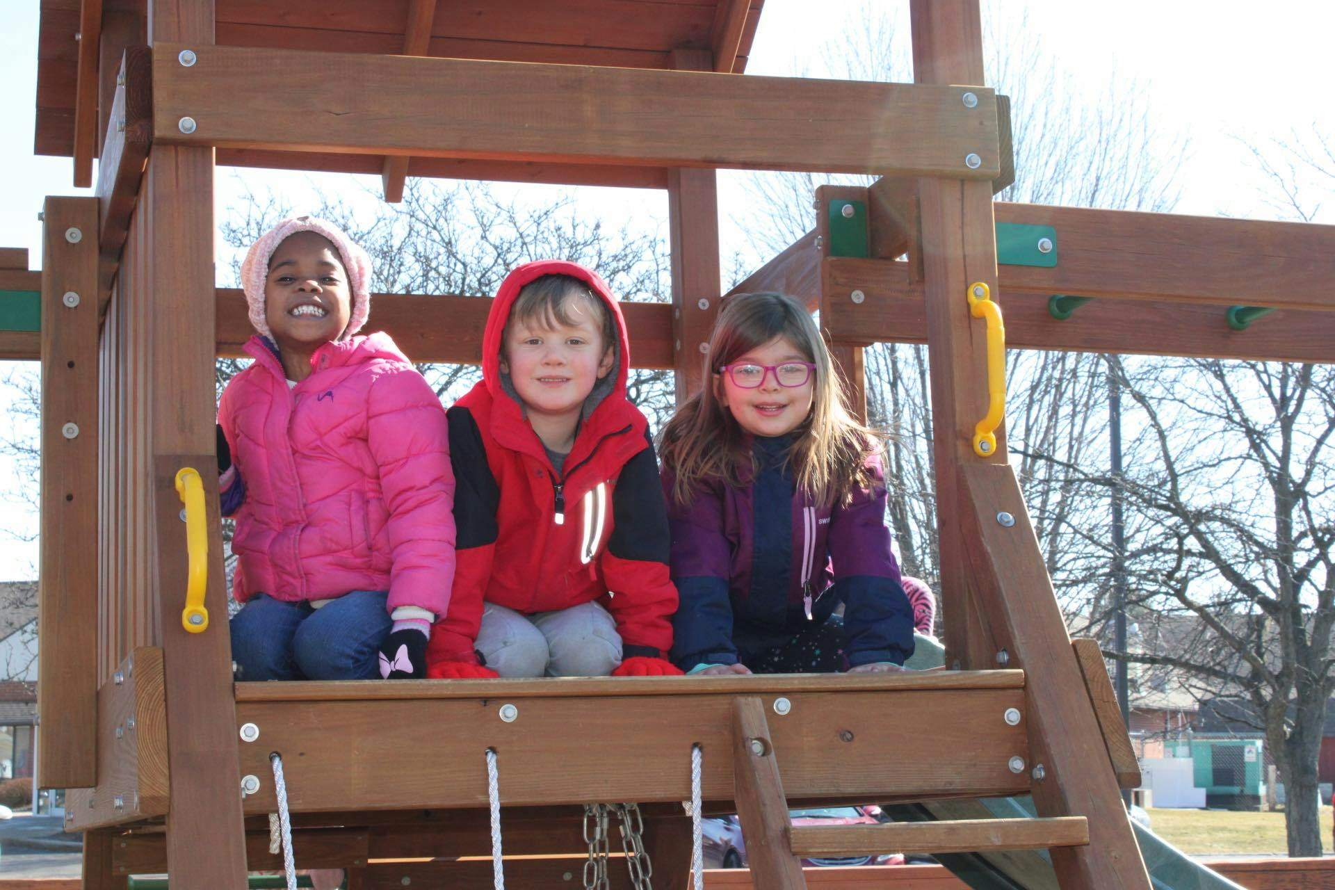 Three children sitting together on a wooden playground structure