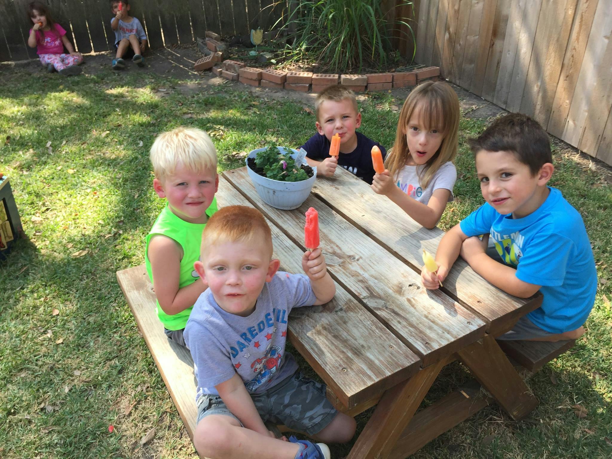 Children sitting at a picnic table eating popsicles