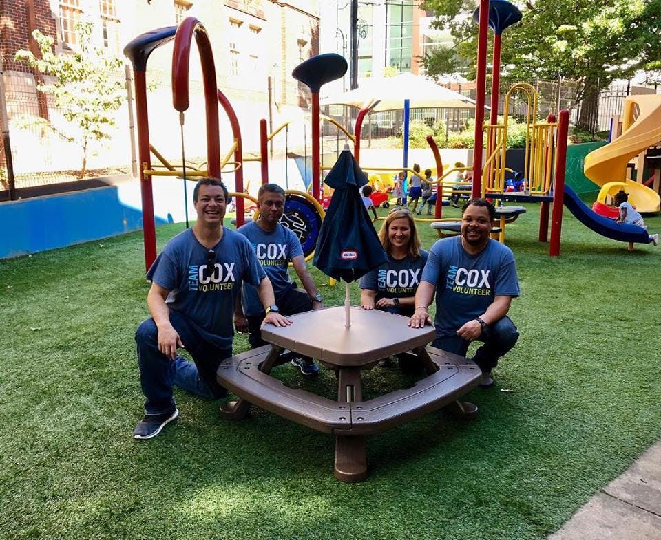 Four people in matching shirts posing around a picnic table on a playground