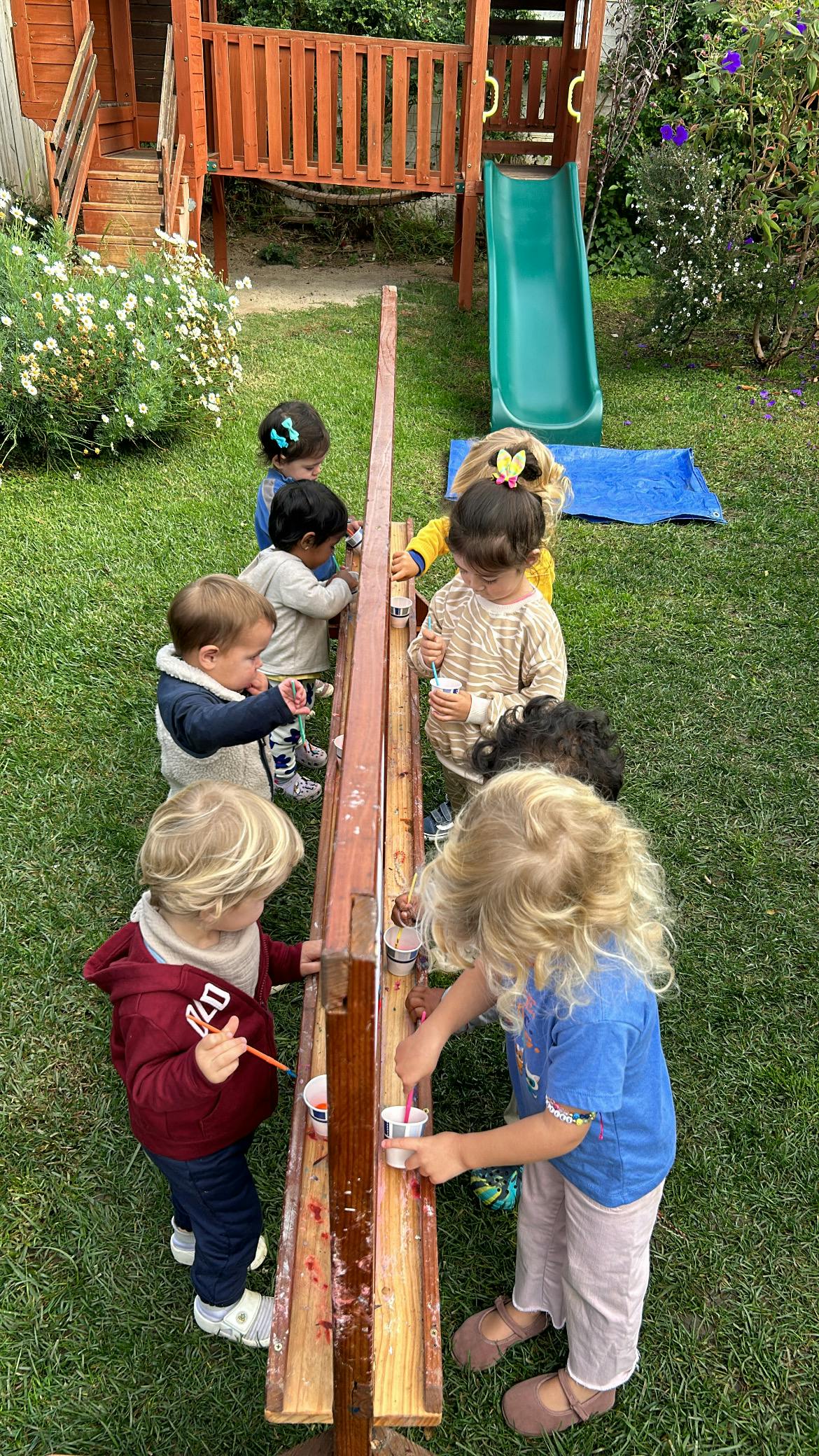 Children painting at a wooden easel outdoors