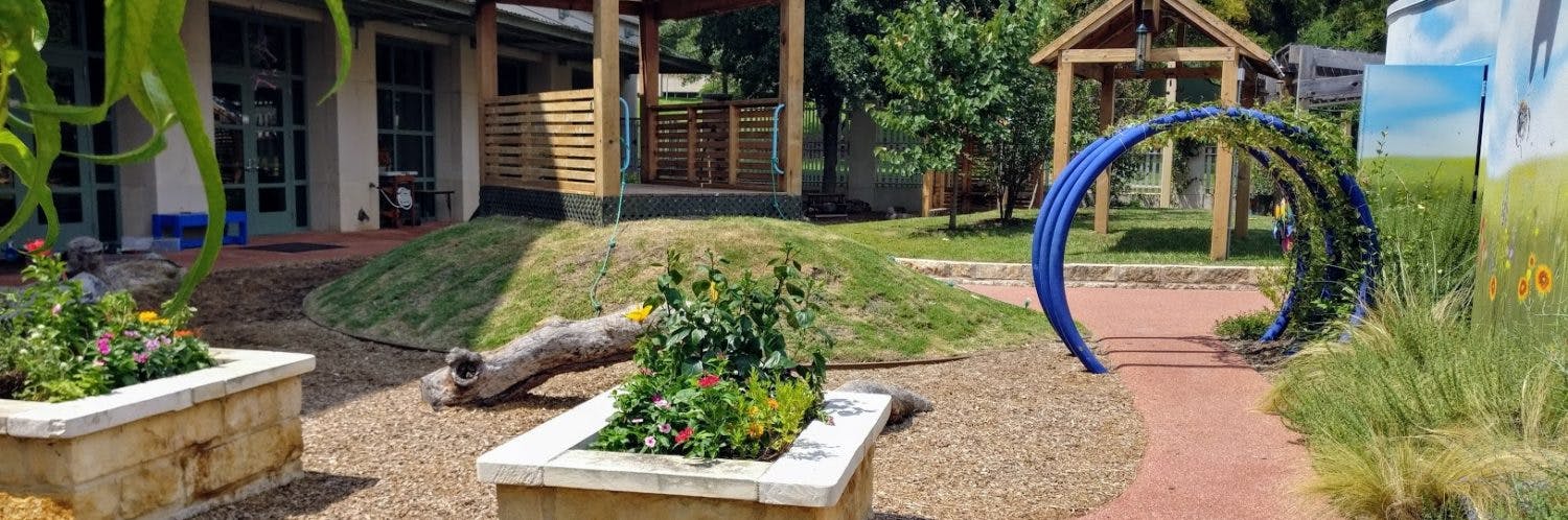 Outdoor play area with planters, a log, and a blue archway