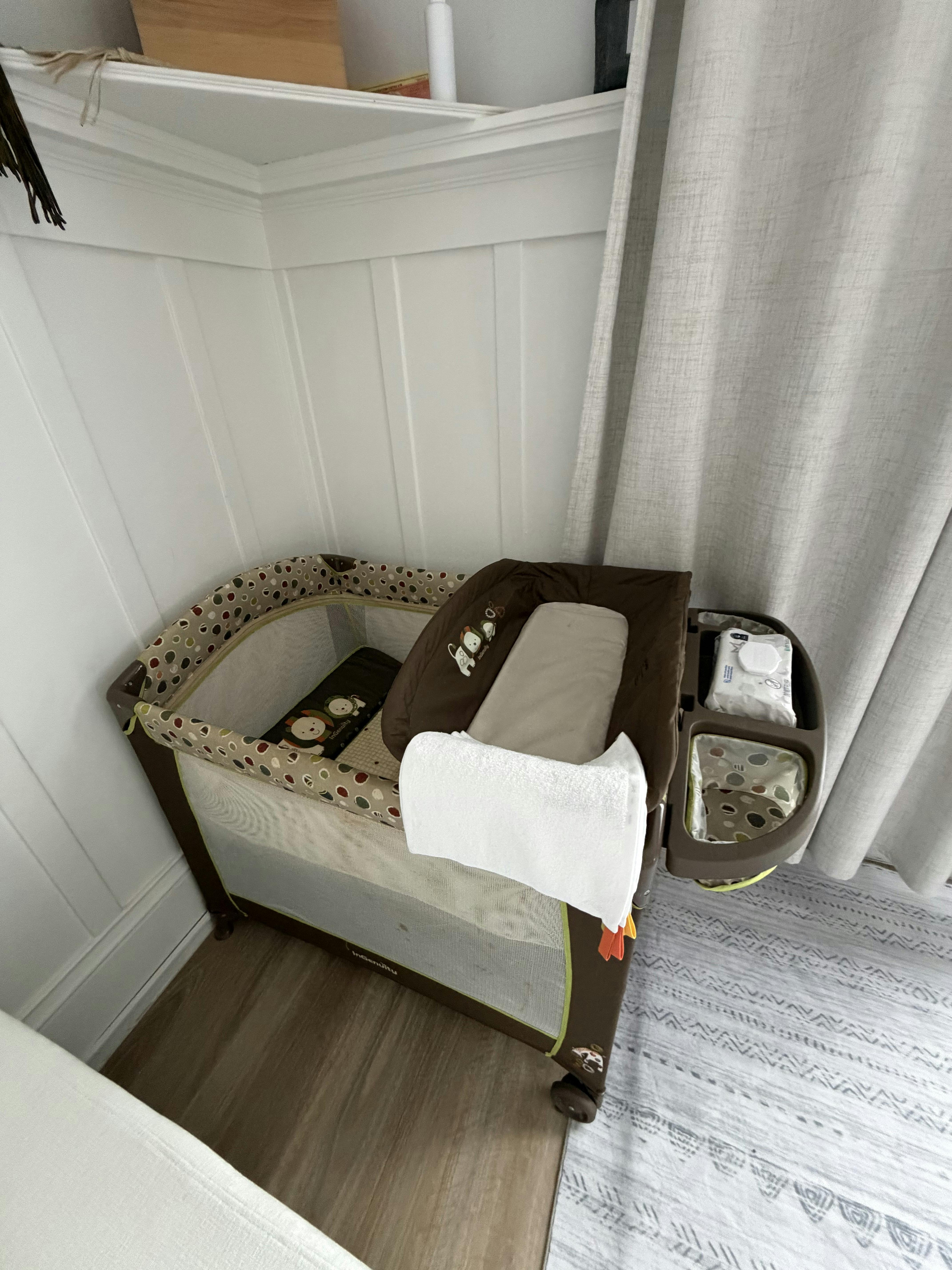 A baby bassinet with changing station next to a white wall and curtain