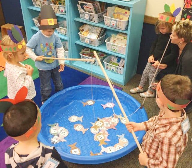 Children playing a fishing game with toy fishing rods and paper fish in a blue pool