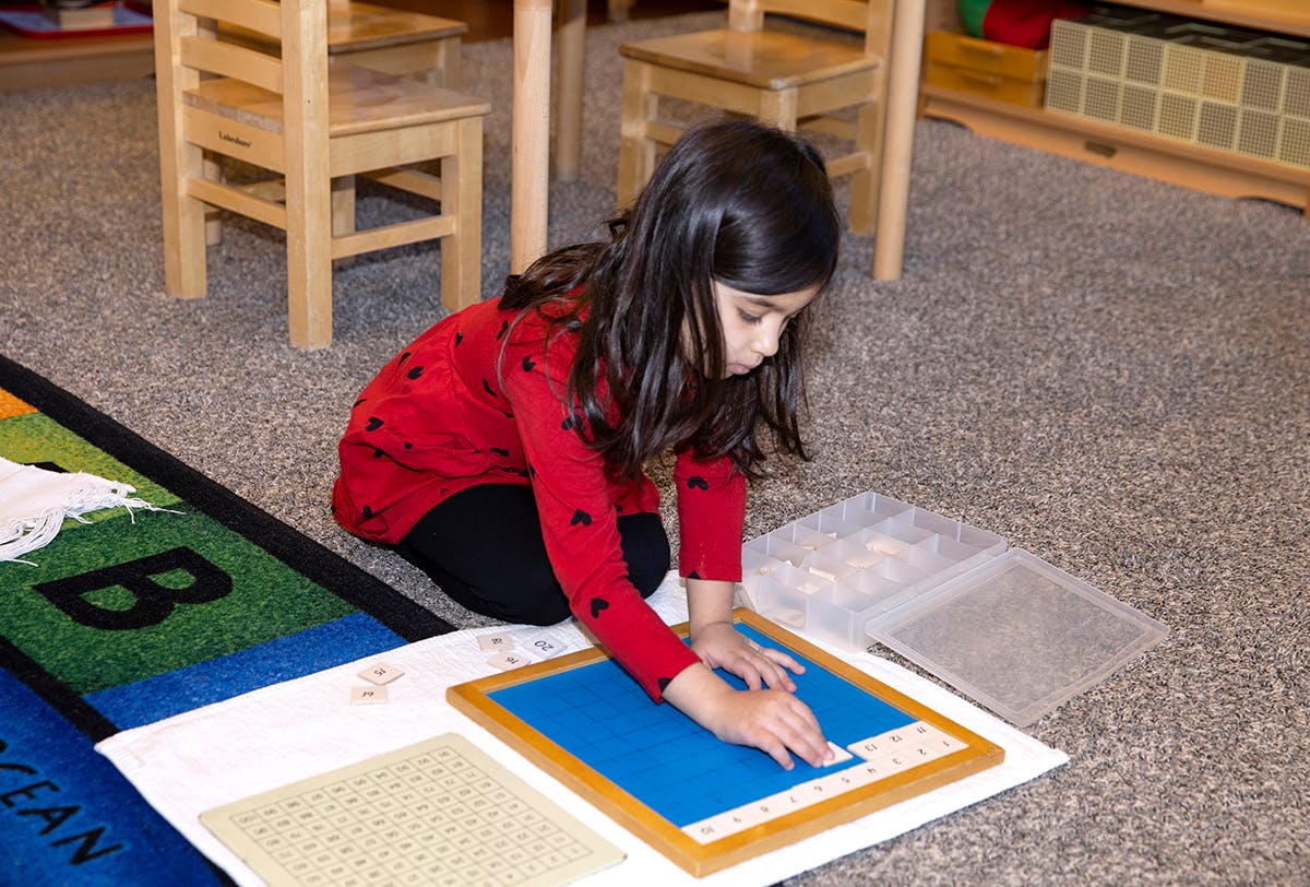 Child kneeling on floor, working with a blue and wood learning board
