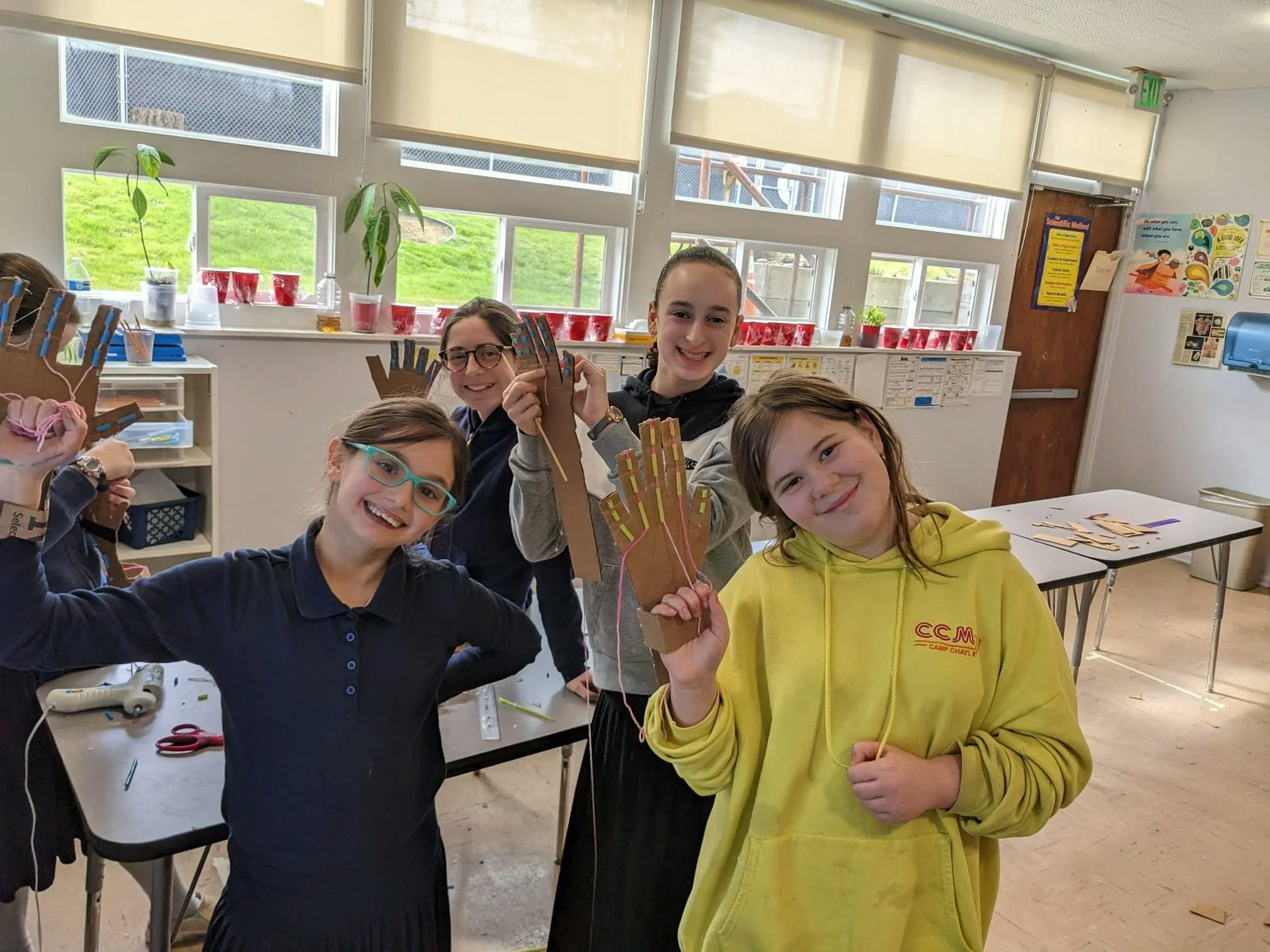 Group of children holding up cardboard hand crafts in a classroom