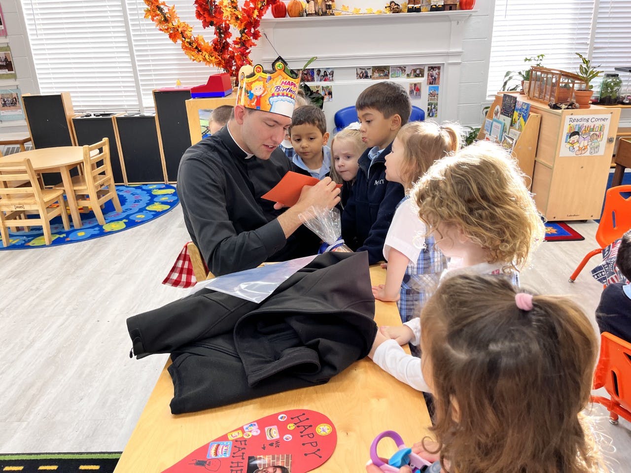 Adult in a paper crown showing something to children in a classroom