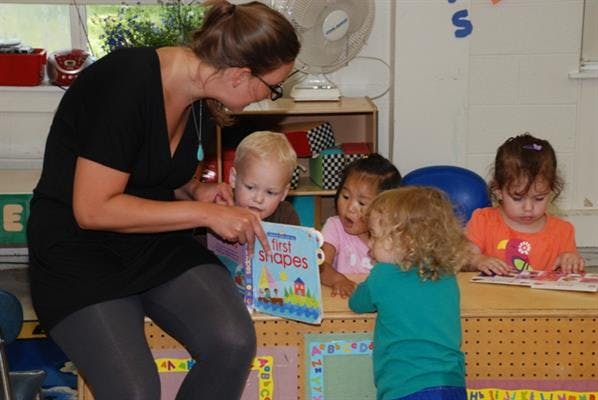 Person reading a book to multiple children in a classroom
