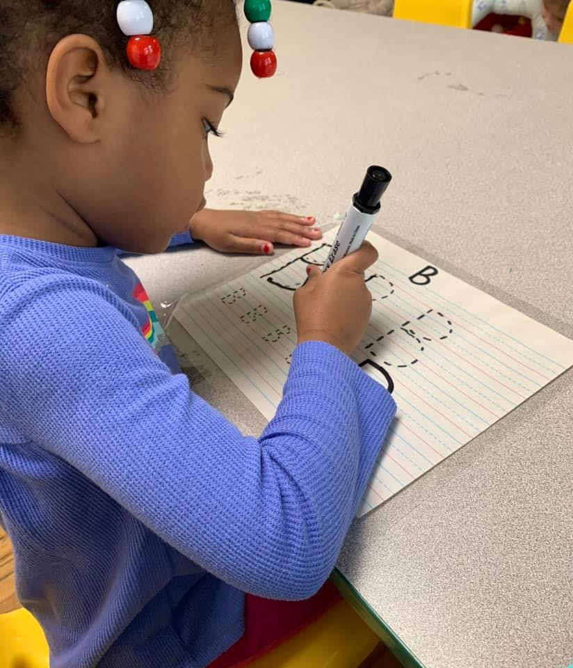 Child tracing letters on paper with a marker