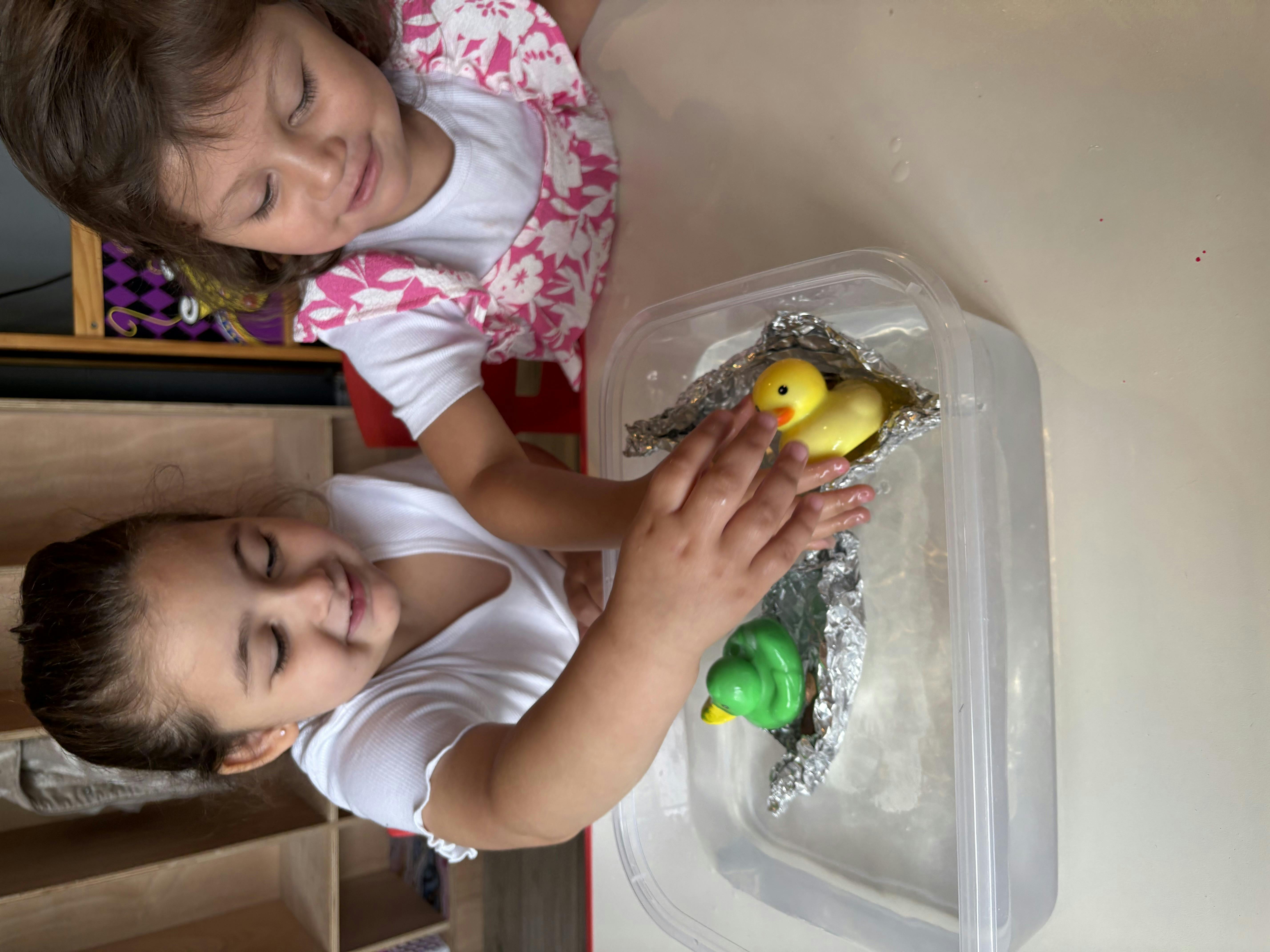 Two children playing with toy ducks in a container of water
