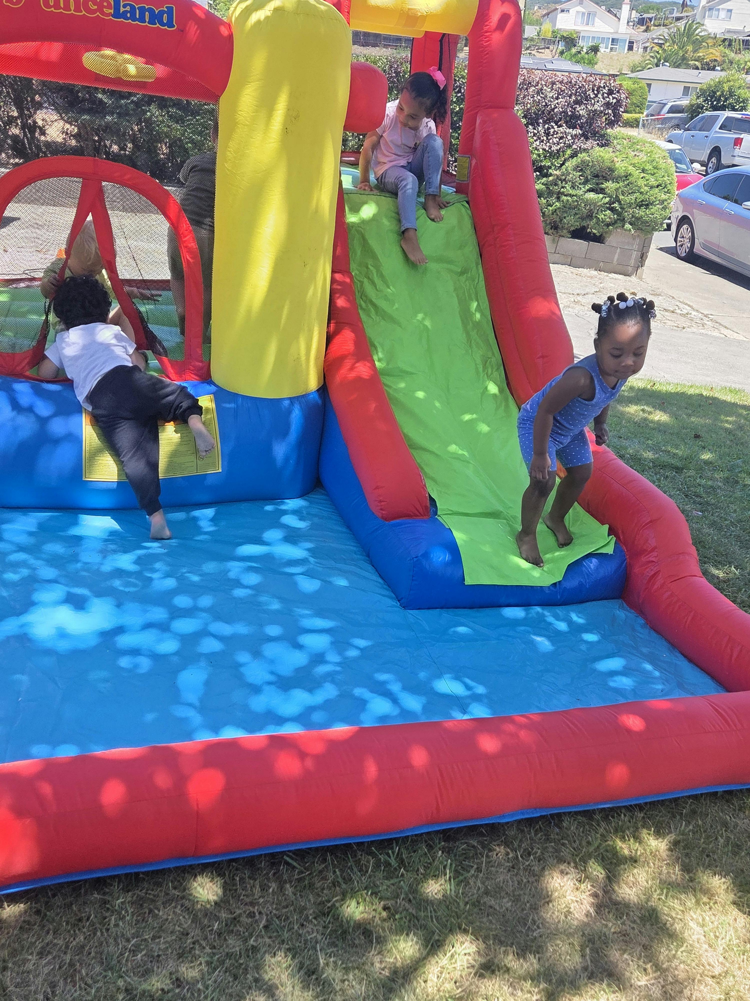 Children playing on an inflatable bounce house with a slide outdoors