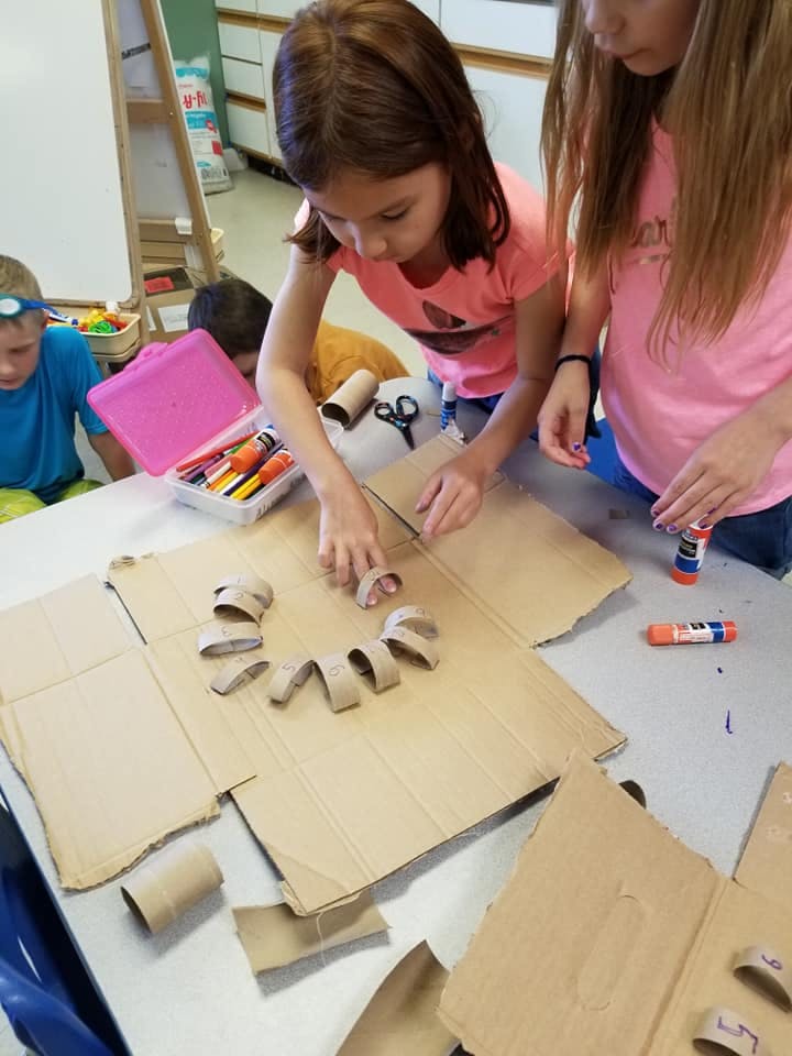 Two children working on a craft project with cardboard and glue
