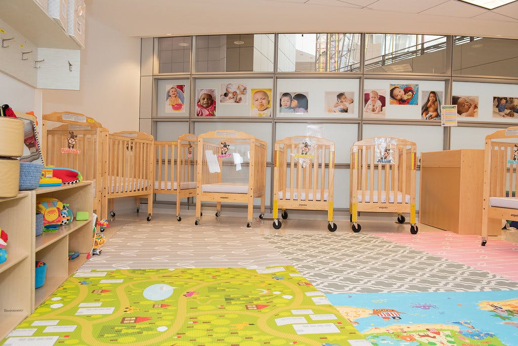 multiple wooden cribs in a room with playmats on the floor and baby photos on the wall