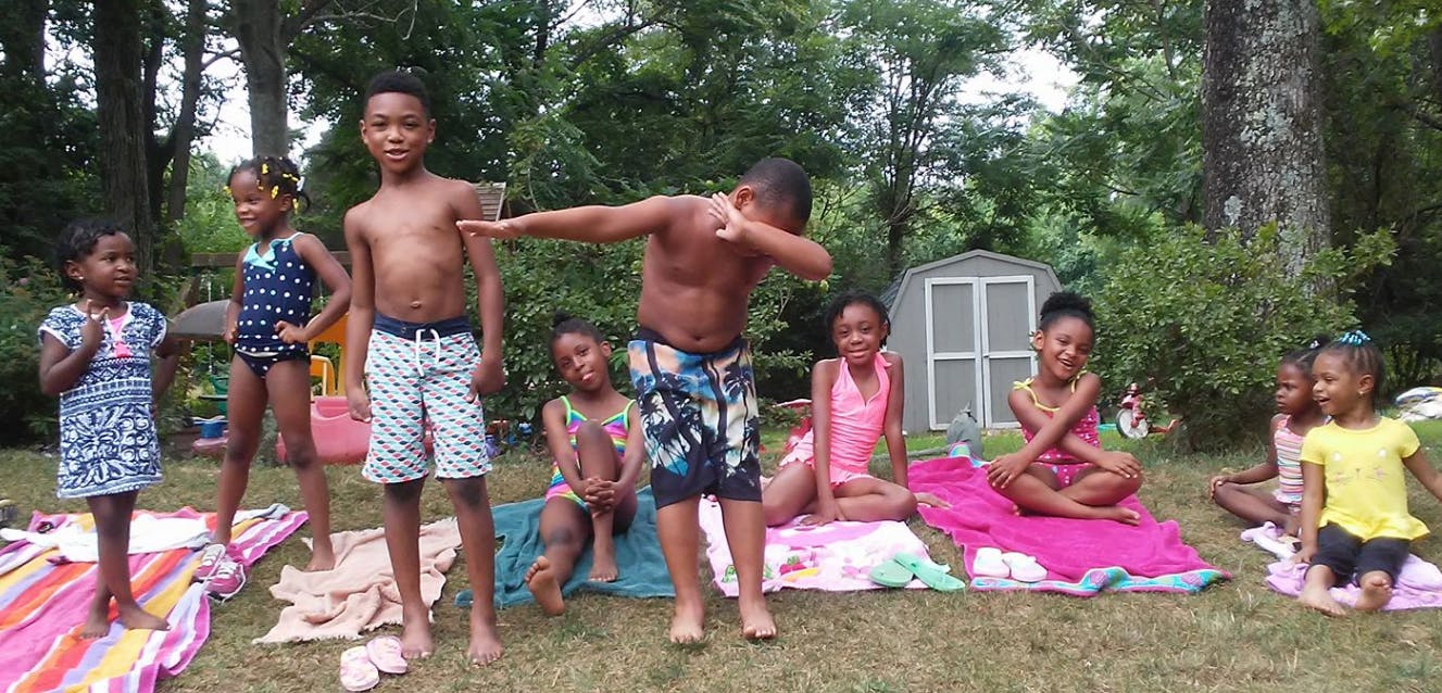 Group of children posing outdoors, one child dabbing