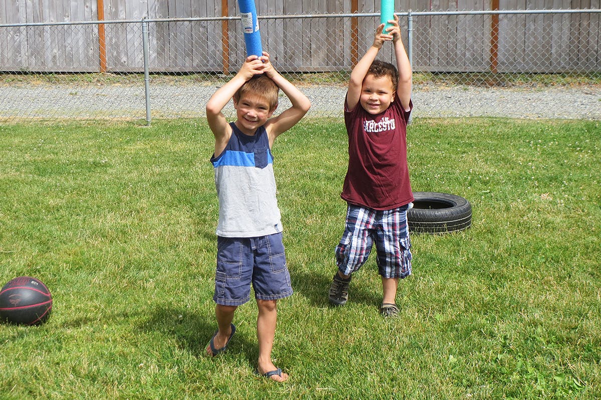 Two children holding blue objects above their heads in a grassy area
