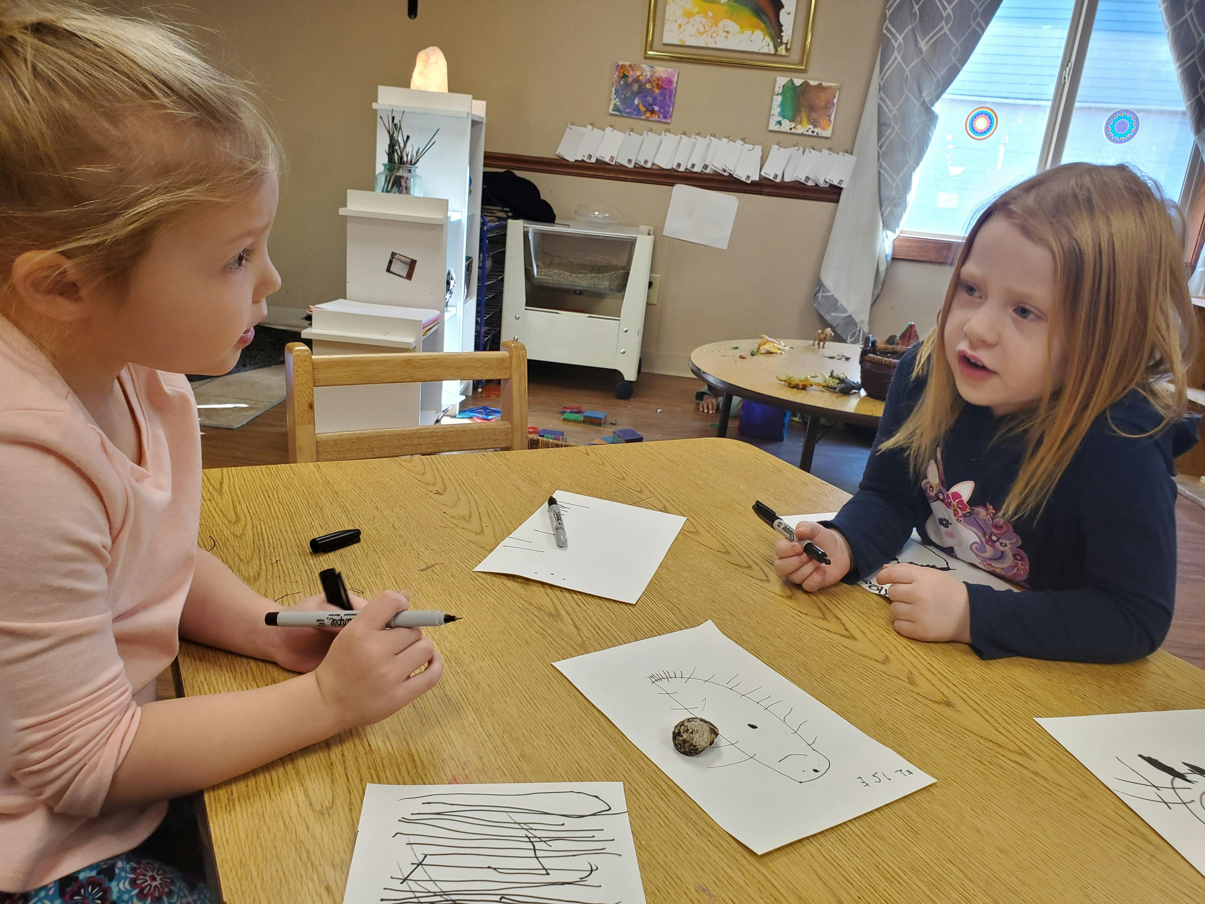 Two children drawing at a table in a classroom