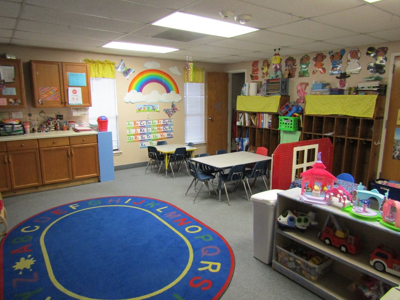 Classroom with small tables and chairs, a rainbow mural, and a blue rug