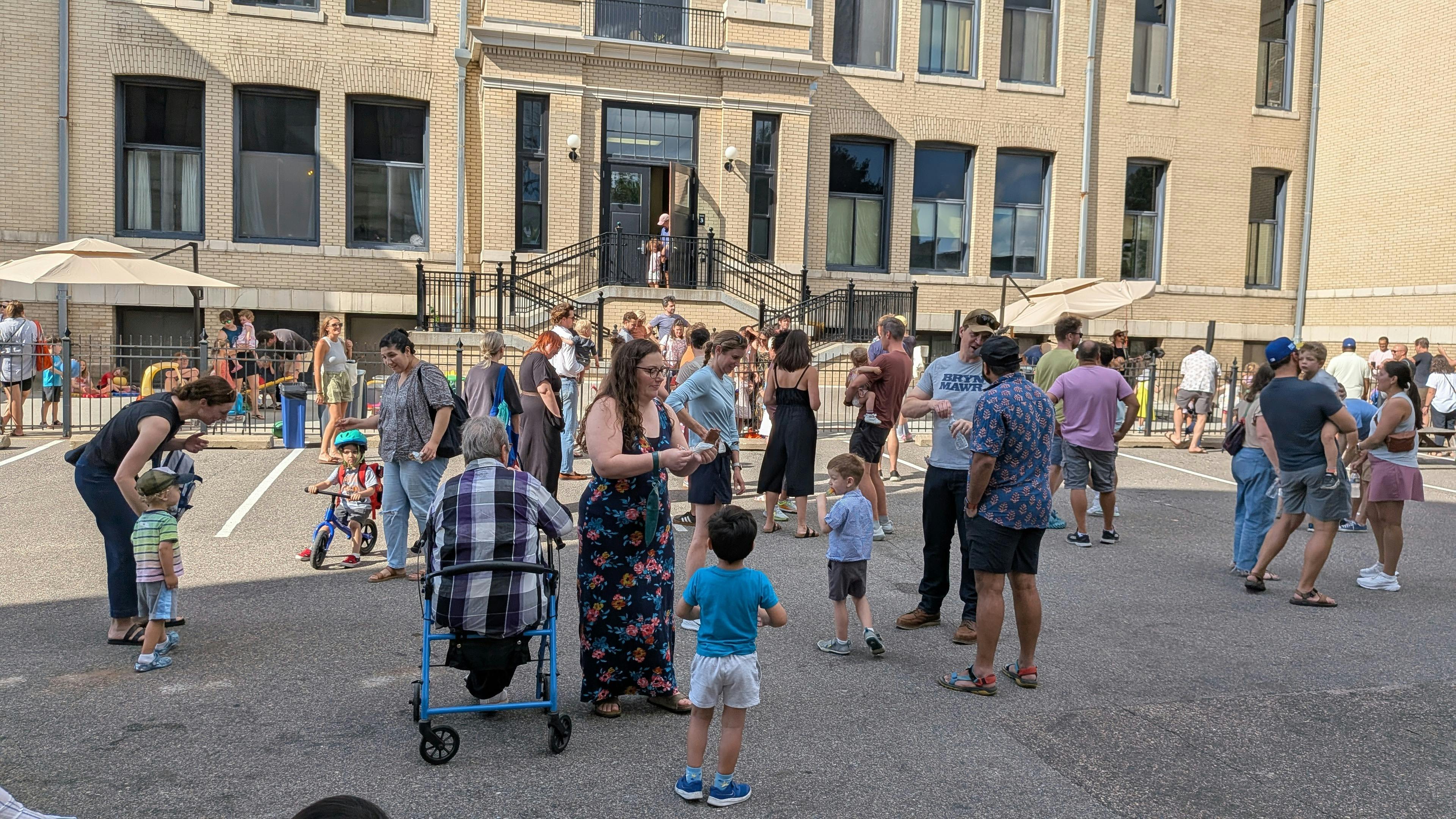 Group of people gathering in a parking lot outside a brick building