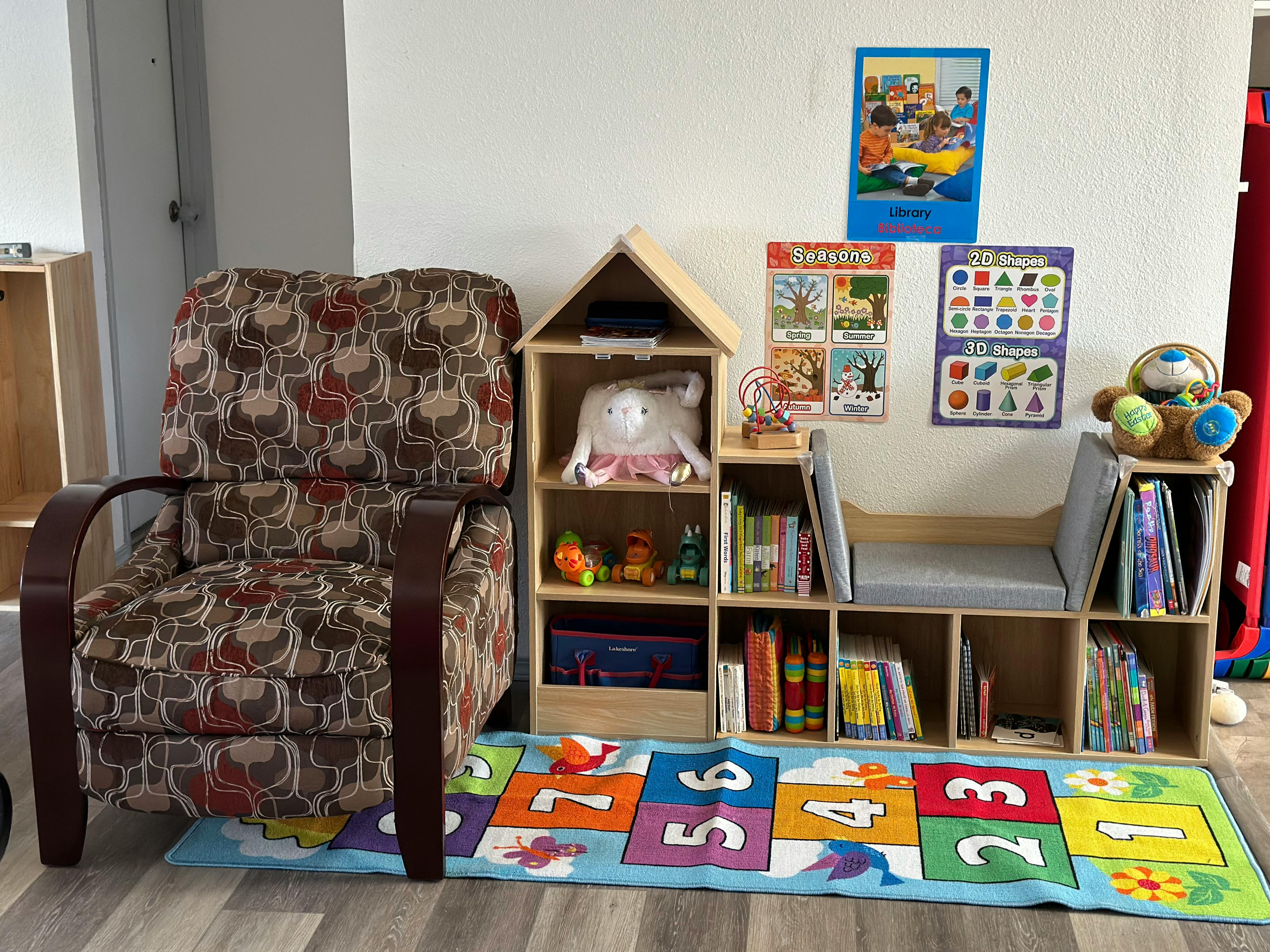 Armchair next to a bookshelf with books and toys, and a colorful rug