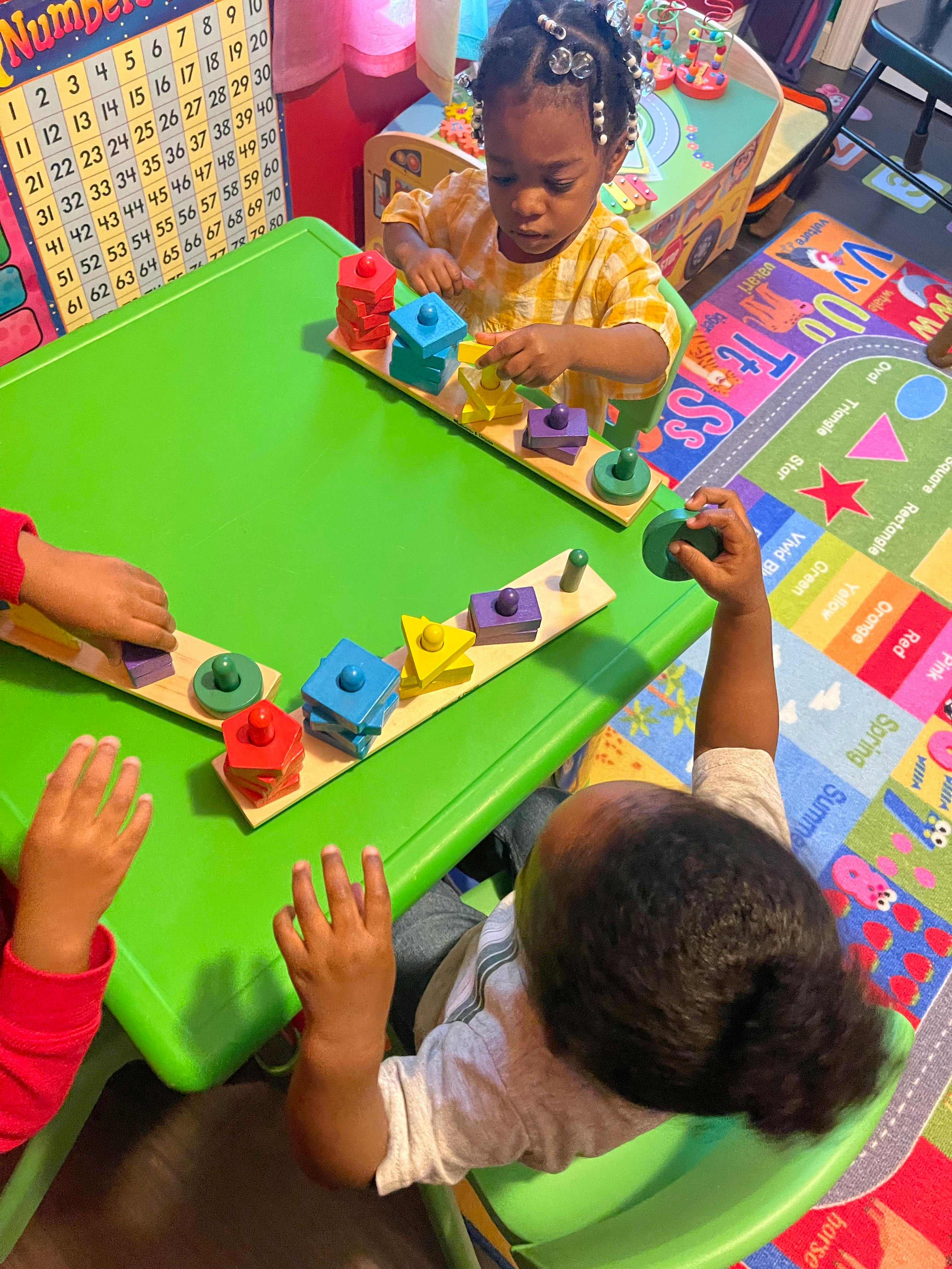 Children playing with shape sorter toys at a green table