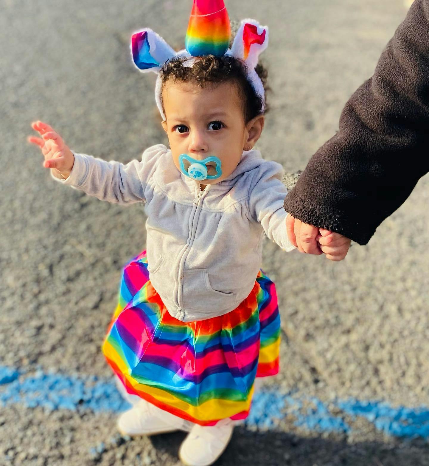 Child in unicorn headband and rainbow skirt holding an adult's hand
